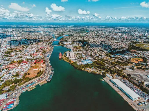 Luftaufnahme einer Stadt mit Fluss, Gebäuden und grünen Flächen unter einem blauen Himmel.